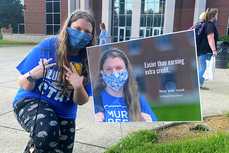 MTSU senior visual communication majors Sydney Clendening of Nashville poses next to a “Defend True Blue” promotional campaign sign featuring her photo outside the university's Business and Aerospace Building. Clendening was part of the MTSU School of Journalism and Strategic Media student team who created a public relations and advertising campaign to encourage their fellow students to wear their masks on campus. The campaign slogan, "Wear Your Mask. Defend True Blue," is included on each image. (MTSU photo by Leslie Haines)