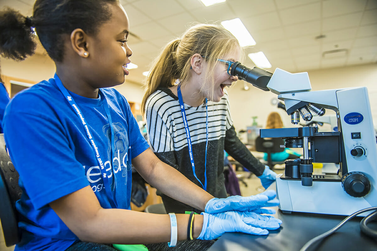 While her lab partner, left, watches, a middle school girl participating in an Expanding Your Horizons workshop in February 2018 in the MTSU Science Building reacts while viewing what's under the microscope. (MTSU file photo by Eric Sutton)