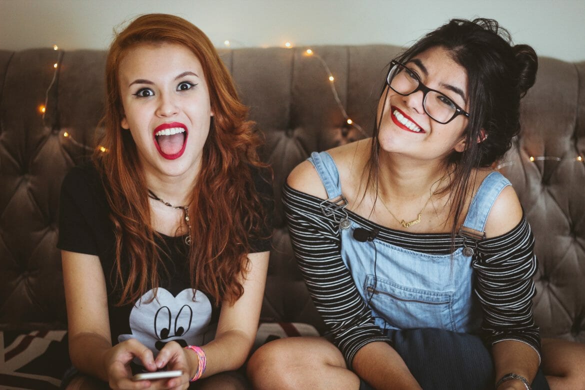 Photo of two women sitting on a couch smiling. Photo by Matheus Ferrero on Unsplash.