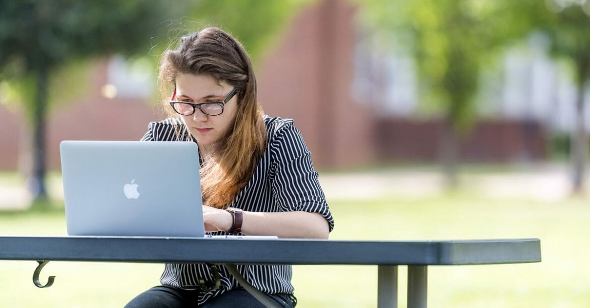 MTSU student sitting at a picnic table on campus working on her laptop computer.