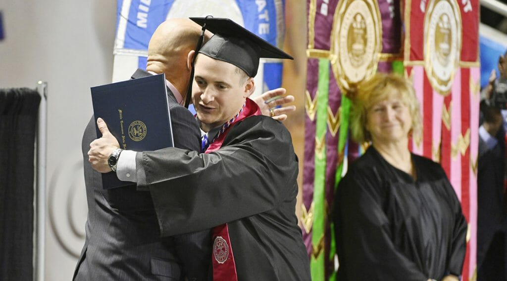U.S. Army veteran Jay Strobino, new bachelor's degree in exercise science in hand, gets a hug from retired U.S. Army Lt. Col. Keith Huber, left, as Huber's assistant, Pat Thomas, looks on during MTSU's fall 2018 afternoon commencement ceremony in Murphy Center. Huber, MTSU's senior adviser for veterans and leadership initiatives, has been advising Strobino on post-graduation career options with the help of the Charlie and Hazel Daniels Veterans and Military Family Center on campus. (MTSU photo by Andy Heidt)