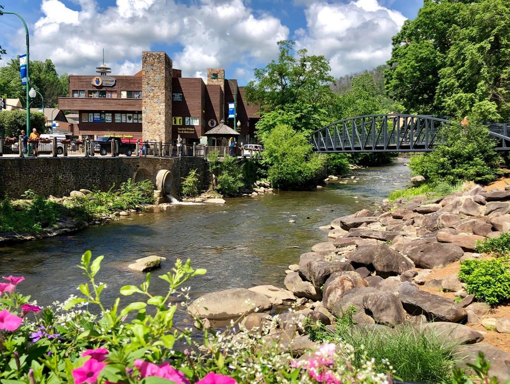 Photo of Gatlinburg stream running under bridge during spring day with flowers and rocks in the foreground and building in the background. Photo from Visit Gatlinburg's Facebook page