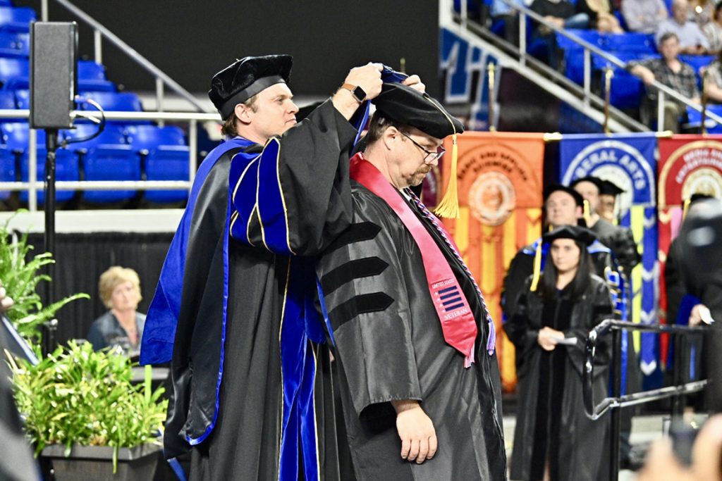 Dr. Cyrille Magne, an MTSU associate professor in literacy studies, helps MTSU graduate Perry Louden don the hood signifiying his new doctoral degree during the Friday, May 3, spring 2019 College of Graduate Studies commencement ceremony at Murphy Center. Louden, a Rutherford County Schools teacher, earned his doctorate in literacy studies, his fourth MTSU degree. MTSU awarded 384 master’s and doctoral degrees in the May 3 ceremony and will present 2,145 undergraduates with their diplomas in dual ceremonies Saturday, May 4. (MTSU photo by J. Intintoli)