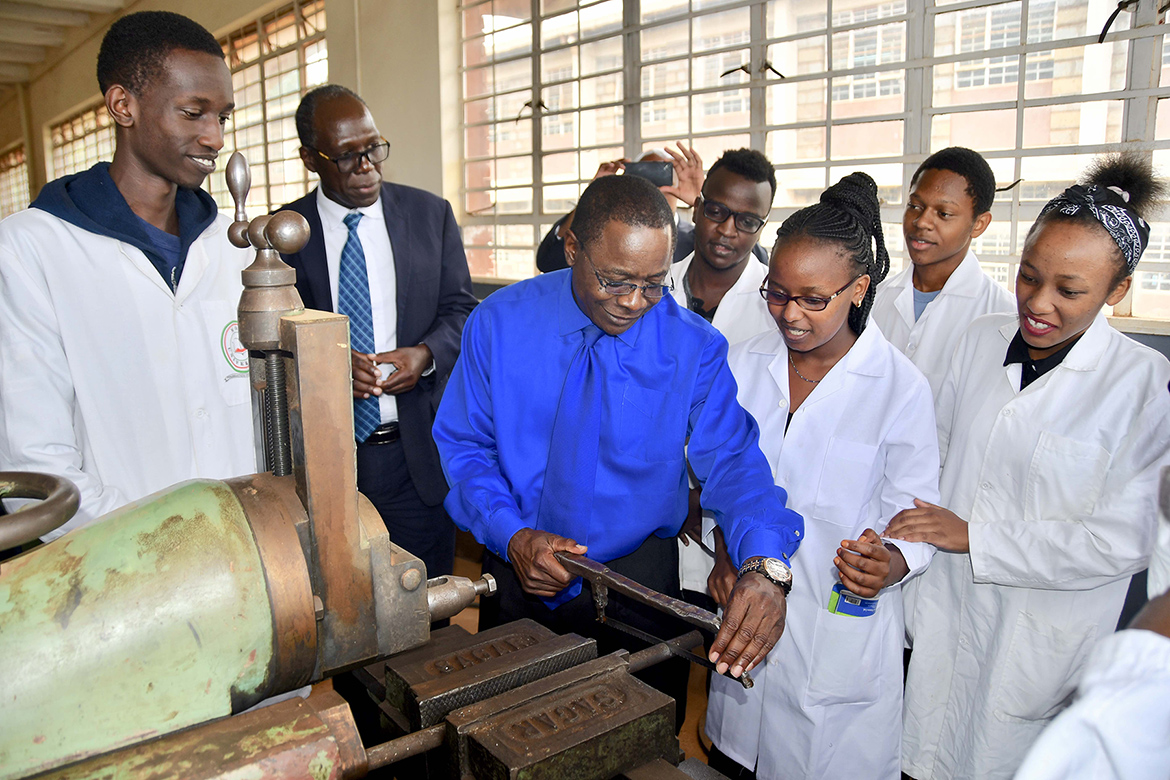 MTSU President Sidney A. McPhee works a hacksaw at an applied engineering laboratory at Moi University in Kenya as students watch. (MTSU photo by Andrew Oppmann)