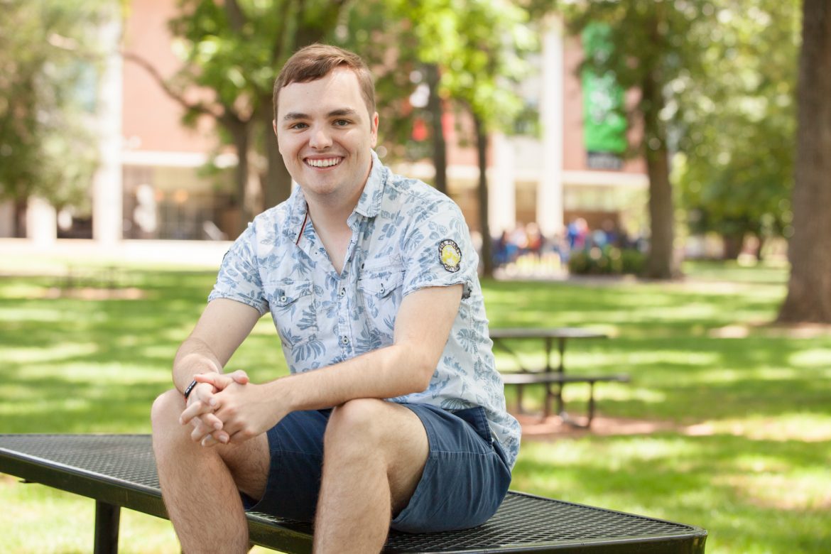 Kobe Hermann, a first-generation MTSU student from Chattanooga, Tennessee, sitting on a table in Walnut Grove. Photo by John Goodwin.