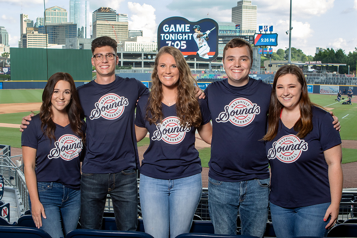 MTSU students serving as brand ambassadors for the Nashville Sounds this season pose in the stands in front of the field and scoreboard. Pictured, from left, are Emily Undieme, Cody Gentile, Mary Ruth Wheeler, Kobe Hermann and Jessie Steele. (MTSU photo by James Cessna)
