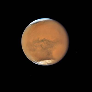 A Hubble Space Telescope photograph of Mars on July 18, 2018. Polar ice caps and atmospheric dust storms are evident in this image. The two Martian moons, Phobos (right) and Diemos (left) are seen in the lower half of the image. (NASA photo)