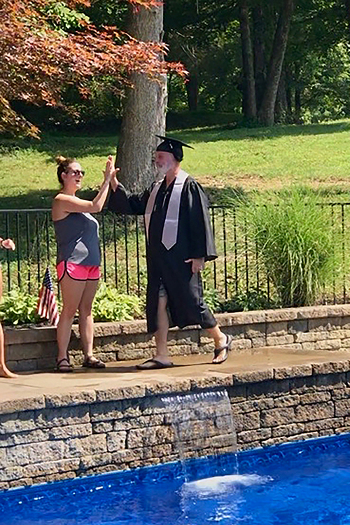 Dressed in cap and gown, Trey Lee, right, assistant superintendent of engineering and construction for Rutherford County Schools, high-fives a family member in a makeshift receiving line at a special graduation ceremony put on by his family in August. The Lee family celebrated Trey's completion of a 30-year journey to earn his degree in construction management at MTSU, made possible by the university’s flexible degree options. (Photo submitted)