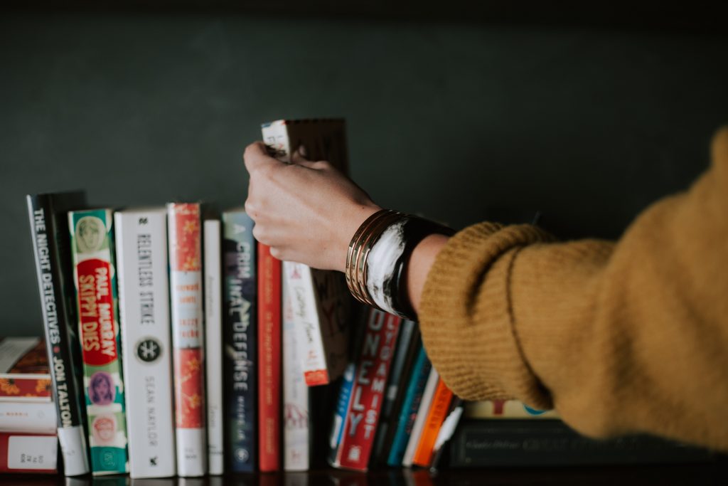 Books lined up with an arm picking one out. Photo by Christin Hume on Unsplash