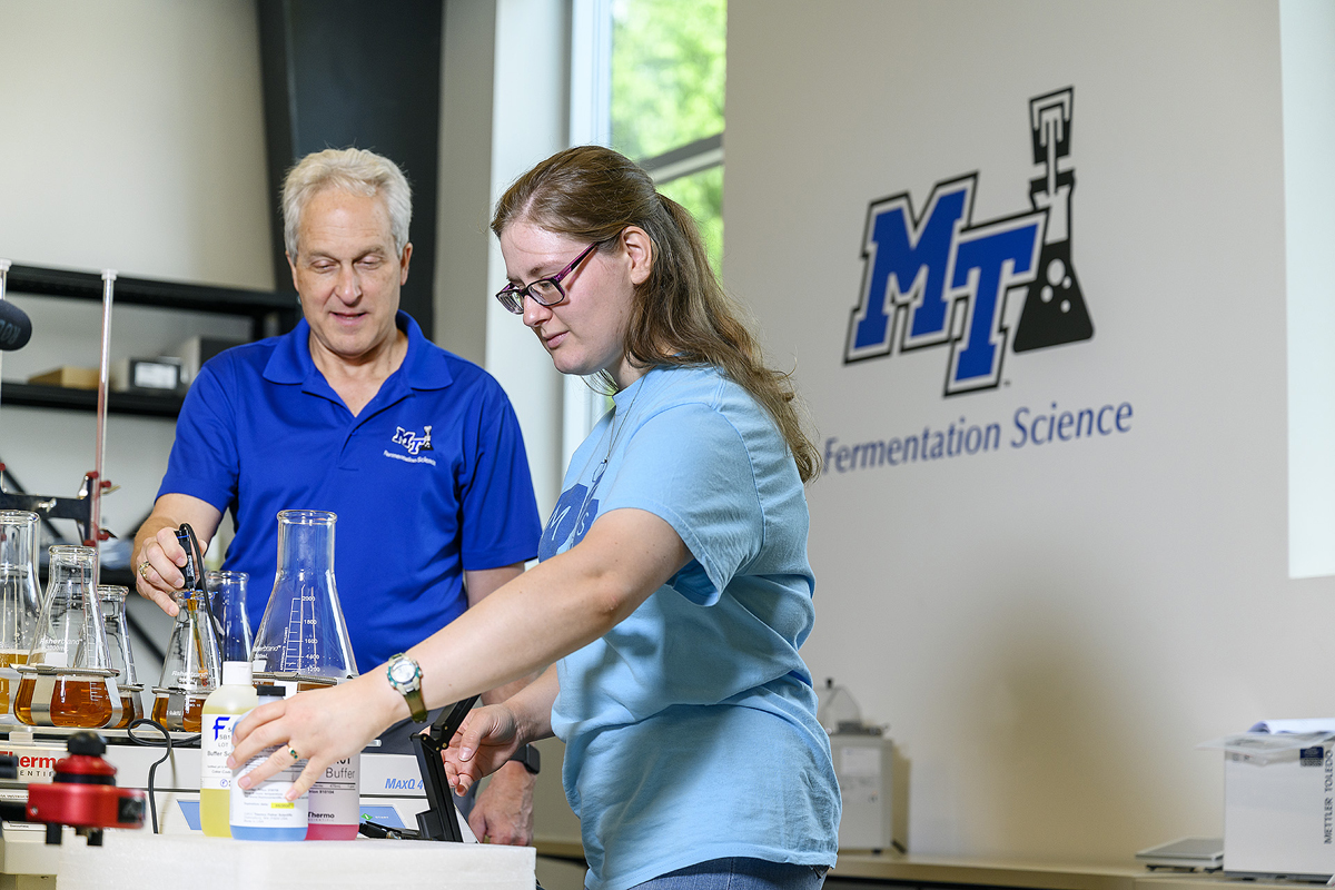 MTSU Fermentation Science Director Tony Johnston, left, oversees as former student and 2019 graduate Kayley Stallings works with ingredients and chemicals in the lab at university partner Hop Springs in Murfreesboro in this 2019 file photo. A three-year, $300,000 U.S. Department of Agriculture grant is an MTSU partnership with Motlow State and Columbia State community colleges, to help recruit students to agriculture and fermentation science. (MTSU file photo by J. Intintoli)