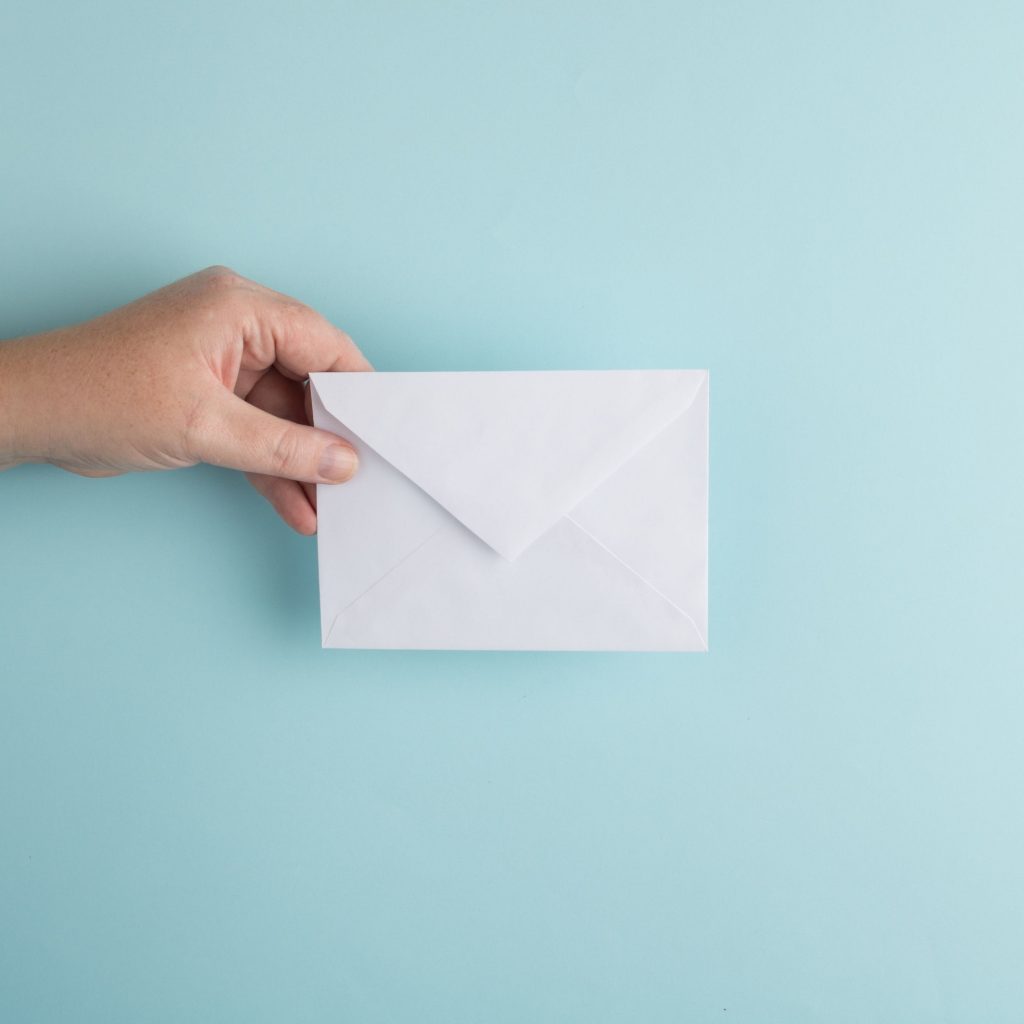 Hand holding an envelope over a blue background. Photo by Erica Steeves on Unsplash