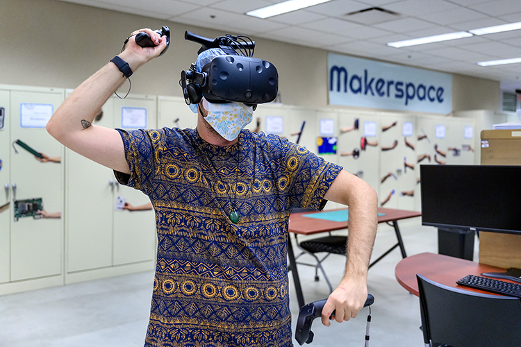 Keri LaPrairie, a student worker at Makerspace, demonstrates the virtual reality device. LaPrairie is wearing a hair covering and an additional mask between his face and the goggles to adhere to COVID-19 protocols. (MTSU Photo by J. Intintoli)