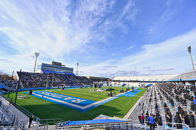 Graduating MTSU students stand, safely distanced and masked, under bright blue skies on the east side of Floyd Stadium, right, for the national anthem Saturday, Nov. 21, while their supporters look on from the stadium's west side during the university's fall 2020 commencement ceremonies. MTSU, which held virtual graduations for its May and August graduates because of the pandemic, required strict health protocols for the graduates and limited their guests to help keep the open-air event safer. (MTSU photo by Cat Curtis Murphy)