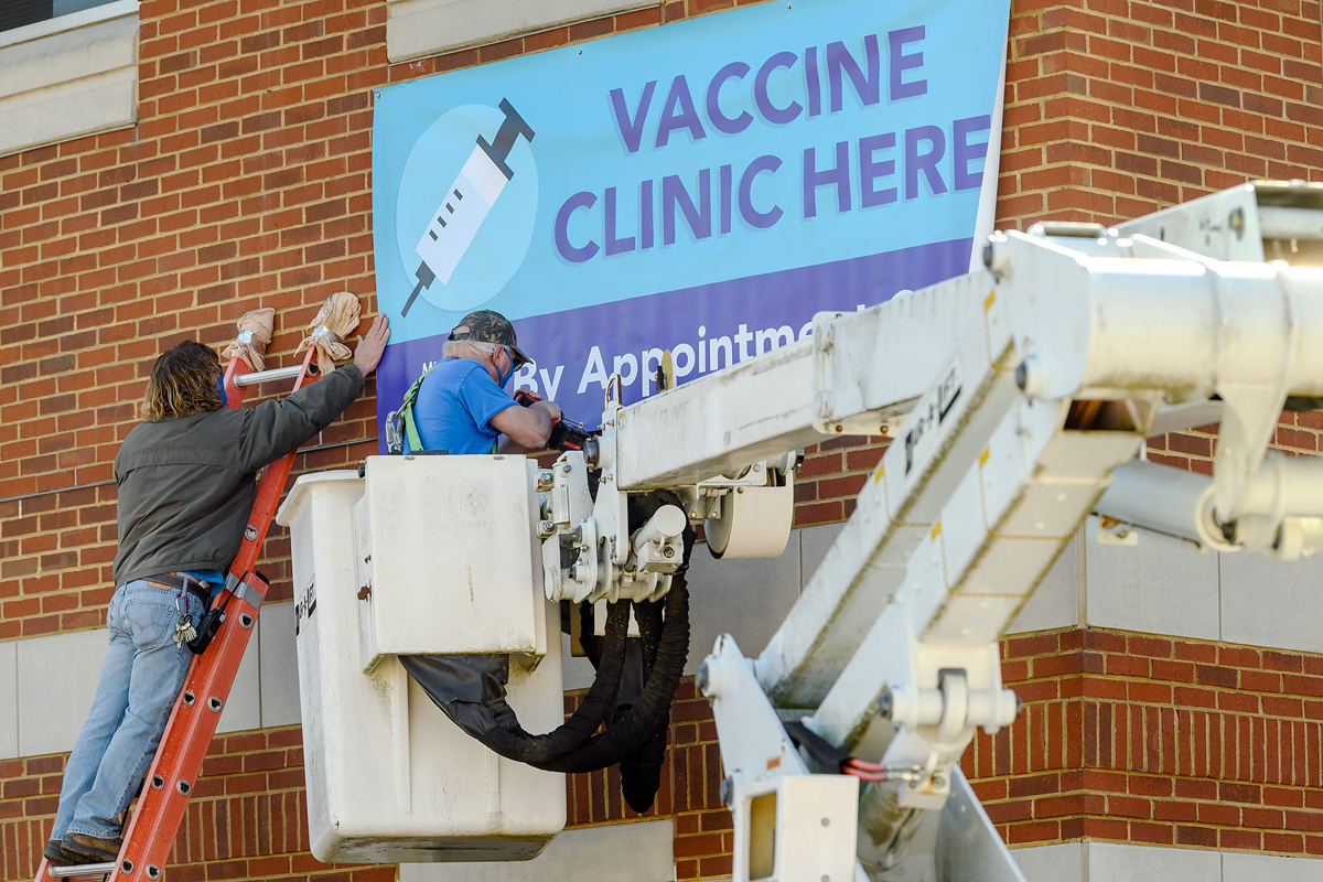 MTSU Building Services employees Forrest Higginbotham, left, and Keith Lawwell hang a banner at Cason-Kennedy Nursing Building on Wednesday, Feb. 24. Along with other banners and yard signs, this will help promote the School of Nursing offering free COVID-19 vaccines to eligible residents by appointment only starting Feb. 25 in CKNB, 610 Champion Way. It is a partnership with the Rutherford County Health Department. (MTSU photo by J. Intintoli)