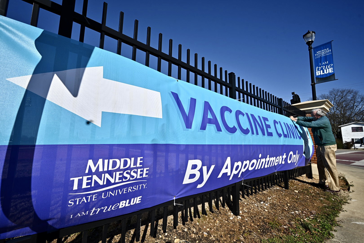 Ed Arning, director of market development for the MTSU Division of Marketing and Communications, secures a large banner to a fence on Blue Raider Driver near Greenland Drive on Wednesday, Feb. 24. It will be signage helping direct traffic to Cason-Kennedy Nursing Building, which will be a new COVID-19 vaccine site in a partnership between the School of Nursing and the Rutherford County Health Department. The vaccine for eligible residents will be available on Thursdays and Saturdays starting Feb. 25. (MTSU photo by J. Intintoli)