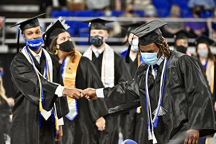 Two members of MTSU’s first Class of 2021 briefly reach out to each other while preparing to cross the stage in Murphy Center during the university’s spring 2021 commencement ceremonies in May. Students will return to Murphy Center Saturday, Aug. 7, for MTSU’s summer 2021 commencement ceremony. (MTSU file photo by J. Intintoli)