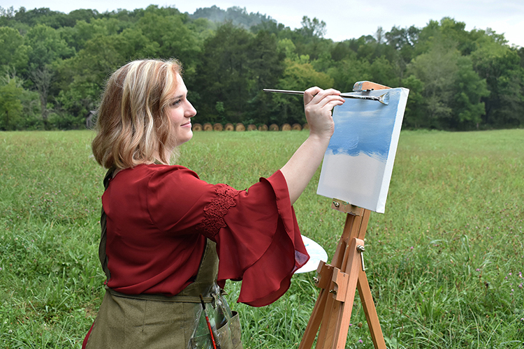 MTSU alumna and artist Catie Adams paints on a new project on canvas in an outdoor setting. She was commissioned to paint a special “Educated Here, Employed Here” print that has been given to 700 MTSU employees who graduated from the university. (Photo by Lynn Adams)