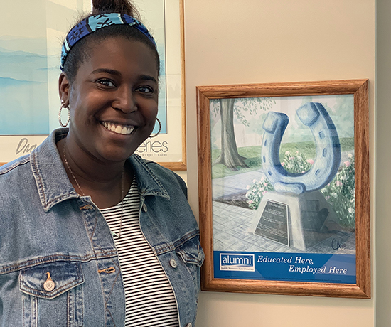 Ashley White, executive aide in the Campus Recreation Center, stands next to a framed print of the “Educated Here, Employed Here” artwork by MTSU alumna Catie Adams and given to 700 employees who earned their degrees from the university. (MTSU photo by Randy Weiler)