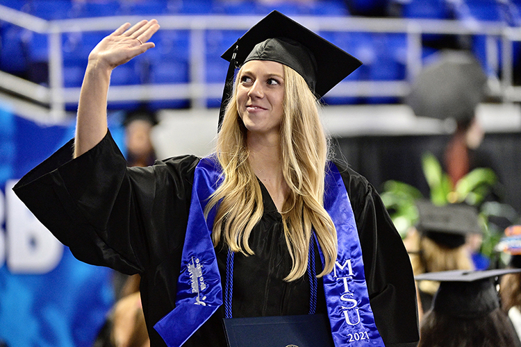 A new MTSU Class of 2021 graduate waves to a supporter as she makes her way across the stage with her degree in Murphy Center at the August commencement ceremony. She's wearing a special custom departmental stole denoting her new degree in exercise science from the College of Behavioral and Health Sciences. MTSU students graduating Saturday, Dec. 11, in the fall 2021 commencement can purchase and wear special new stoles from the university's Phillips Bookstore representing their colleges. (MTSU file photo by Andy Heidt)