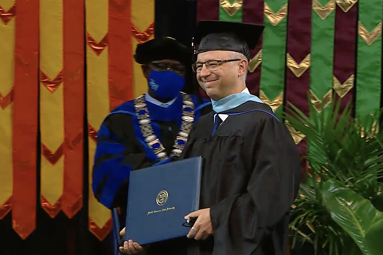 Patrick Toth, 55, a teacher at Page High School in Williamson County, walks the stage of Murphy Center during the spring 2021 Commencement after receiving his master’s degree in Curriculum and Instruction from the College of Education. (Screen capture from MTSU Livestream)