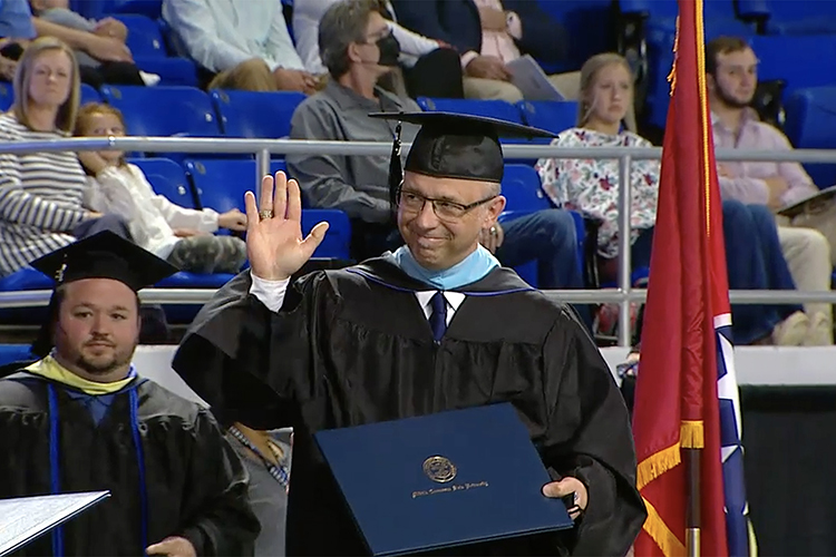 Patrick Toth, 55, a teacher at Page High School in Williamson County, waves to a supporter after walking the stage of Murphy Center during the spring 2021 Commencement to receive his master’s degree in Curriculum and Instruction from the College of Education. (Screen capture from MTSU Livestream)