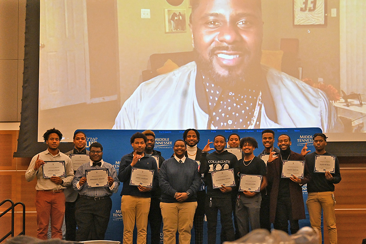 MTSU Scholars Academy Assistant Manager Travis Strattion, center, poses with graduates of the latest Black Male Lecture Series by the Office of Student Success after the closing ceremony held Feb. 18 in the Student Union Ballroom. In the background on the video screen and participating via Zoom is series speaker and former NFL player Jay Barnett, an author, speaker, family therapist and mental health coach who led the participating students through his K.I.N.G. program, which stands for Kindling Innovation Necessary for Growth. (MTSU photo by Jimmy Hart)