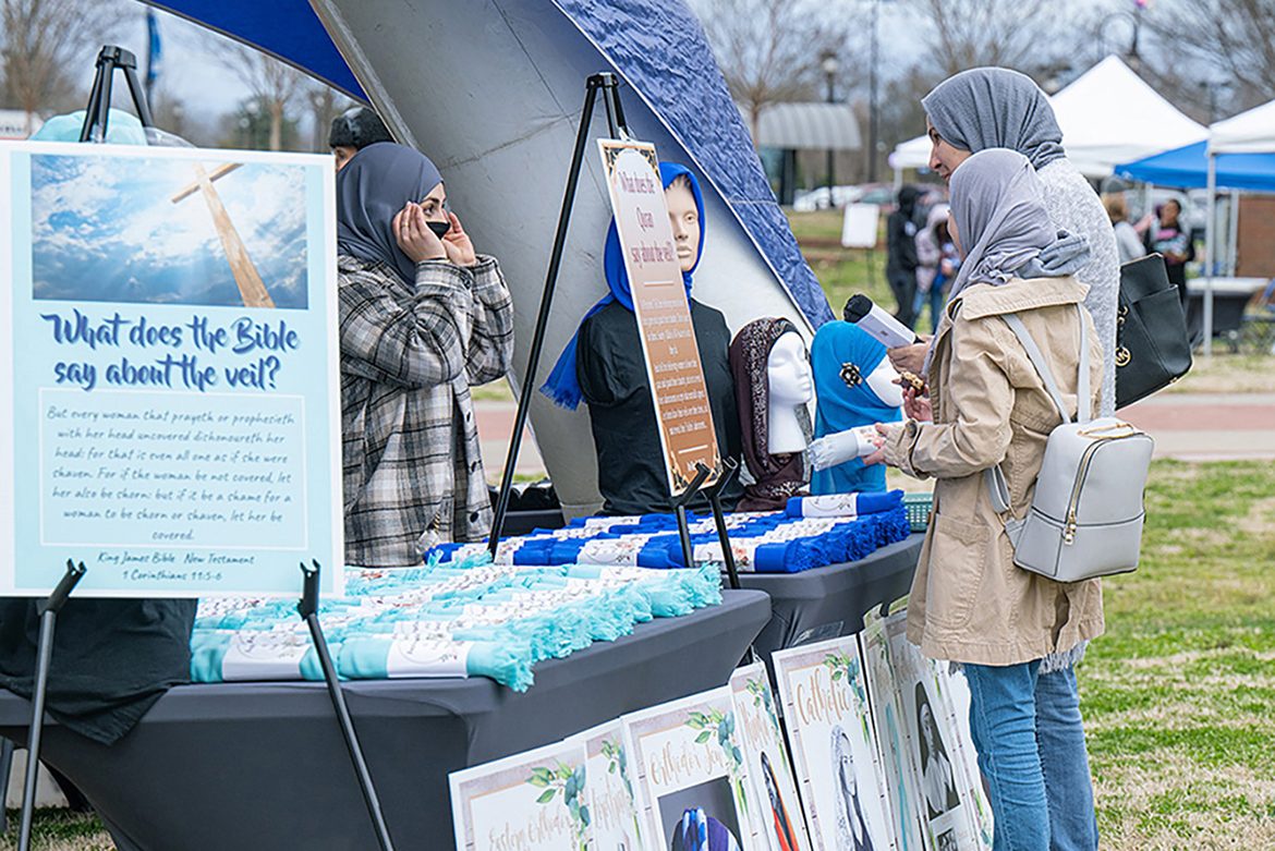 A volunteer explains the hijab, a head covering for Muslim women, to visitors to the Festival of Veils. Posters of various uses of veils in other religions, including Hinduism and Catholicism, are on the grass below tables of free veils. The event was held March 19 on the Student Union Commons. (MTSU photo by Cat Curtis Murphy)