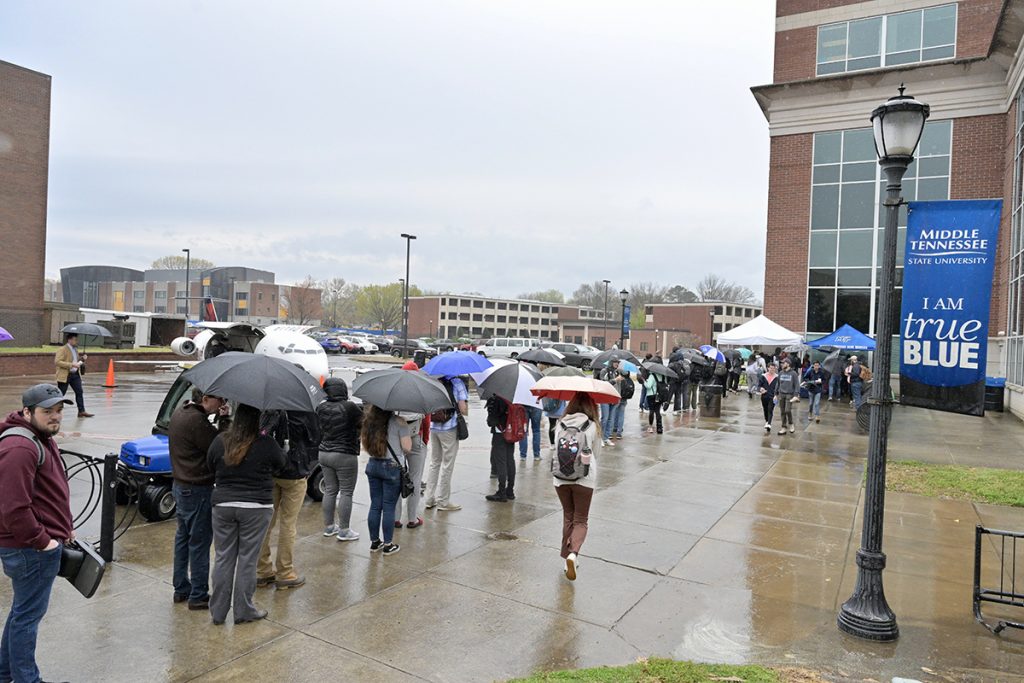 A long line of MTSU students wait in the rain to obtain a free hot dog meal made from the massive, customized Delta Air Lines grill (shown in background) that resembles a small jet near the Quad area next to the James E. Walker Library Tuesday, April 5, following a 30-minute program recognizing Colton Gray of Lebanon, Tenn., as the first graduate in the accelerated Delta Propel pilot program. (MTSU photo by Andy Heidt)