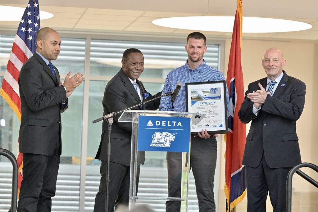 MTSU President Sidney A. McPhee, second from left, presents aerospace alumnus Colton Gray of Lebanon, Tenn., a framed certificate of recognition for becoming the first Delta Propel pilot program graduate, as aerospace Chair Chaminda Prelis, left, and Keith M. Huber, senior adviser for veterans and leadership initiatives applaud with the rest of the audience. MTSU and Delta celebrated the occasion Tuesday, April 5, in the MTSU Science Building’s Liz and Creighton Rhea Atrium. Gray will begin training with Delta on May 10. (MTSU photo by Andy Heidt)