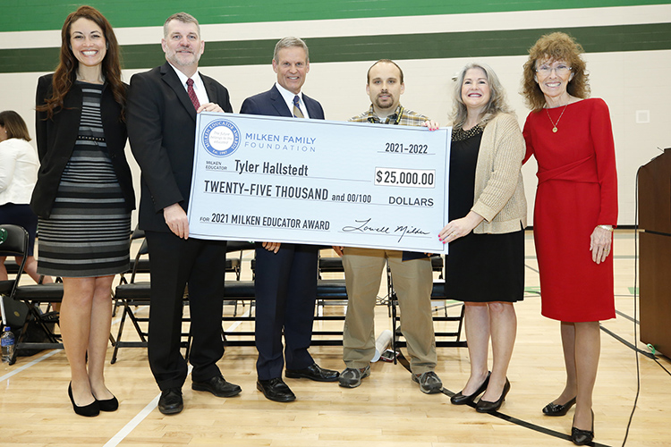 Eighth-grade history teacher and Middle Tennessee State University graduate Tyler Hallstedt, third from right, receives a Milken Educator Award and $25,000 check for being an outstanding teacher at an assembly at Mt. Juliet Middle School in Mt. Juliet, Tenn., on April 7, 2022. Pictured, from left, are Tennessee Commissioner of Education Penny Schwinn, Wilson County Schools Director Jeff Luttrell, Tennessee Gov. Bill Lee, Hallstedt, Mount Juliet Middle School Principal Candis Vandevort Angle and Jane Foley, senior vice president of the Milken Educator Awards. (Photo courtesy of Milken Family Foundation)