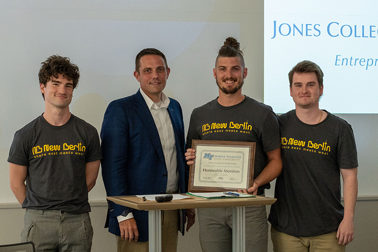 MTSU students Braden Welborn, center right, and partners Tyson and Lucas Sharpe, are presented an honorable mention plaque and $2,000 prize by Joshua Aaron, center left, management professor and holder of the Wright Chair of Entrepreneurship, at the conclusion of the 2022 Business Plan Competition Finals held April 27 in the Academic Classroom Building. The event is presented by the Pam Wright Chair of Entrepreneurship within the Department of Management. The students were recognized for their plan for New Berlin Ventures LLC, a Nashville-based mobile food company that features a Berliner doner kebab. (MTSU photo by Darby Campbell-Firkus)