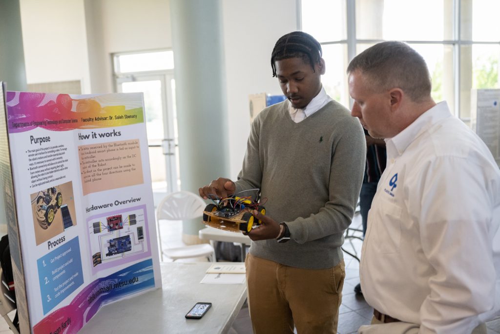Tyson Hardy, left, explains his wireless remote robotic vehicle to an industry partner helping judge the recent MTSU Engineering Technology Mech-Tech Expo in the Miller Education Center’s second-floor atrium. Dozens of mostly seniors showing off their capstone projects participated in the event, which drew more than 200 people. (MTSU photo by James Cessna)