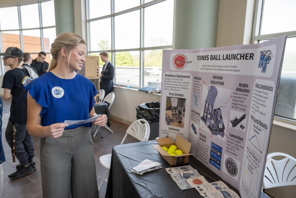 MTSU senior Ashley Dunn of Jackson, Tenn., a mechatronics engineering major, looks at the tennis ball launcher she and teammates created this semester and shown publicly during the spring 2022 Engineering Technology Mech-Tech Expo Thursday, April 28, in the Miller Education Center second-floor atrium. Students who will be graduating May 7 displayed their posters and projects at the event. (MTSU photo by James Cessna)
