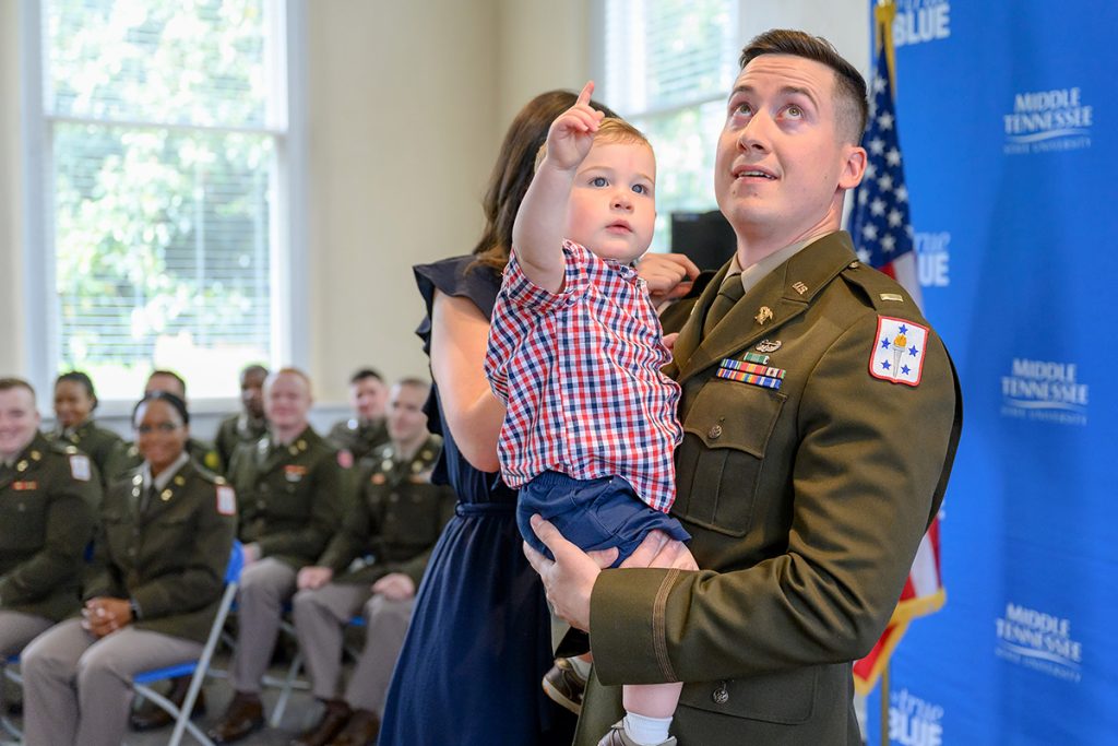 While wife Taylor Maynard, left, pins on his second lieutenant bars on the uniform, newly commissioned Michael Maynard holds their son, Oliver, Friday, May 6, during the MTSU Blue Raider Battalion spring commissioning ceremony in the Tom H. Jackson Building’s Cantrell Hall. (MTSU photo by J. Intintoli)
