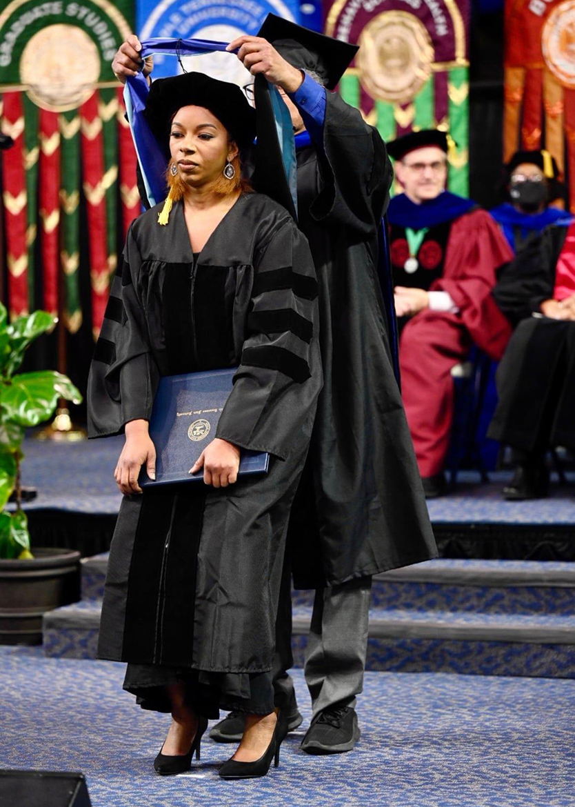 Brelinda Johnson, manager of the MTSU Scholars Academy, steps forward slightly so her dissertation advisor, Donald Snead, can drape her new doctoral hood across her shoulders in December 2021 during fall commencement in Murphy Center. Johnson earned the university's first doctoral degree aimed at helping college students succeed in MTSU's Assessment, Learning and Student Success program. Through a state benefit, university employees can take one class a semester and up to four in one year, and can attend an information session from 11 a.m. to 2 p.m. Thursday, July 28, in the Student Union Atrium to learn more about the educational opportunity. (MTSU file photo by J. Intintoli)