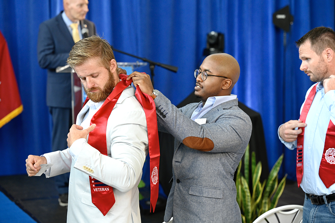 MTSU graduating student veteran Omar Cohen, second from left, helps adjust the red stole worn by fellow senior Nicholas Levitsky Wednesday, July 27, during the summer 2022 Graduating Veterans Stole Ceremony in the Miller Education Center second-floor atrium. At right is James Dikeman. Student veterans receive red stoles they can wear at graduation at 9 a.m. Saturday, Aug. 6, in Murphy Center. (MTSU photo by J. Intintoli)