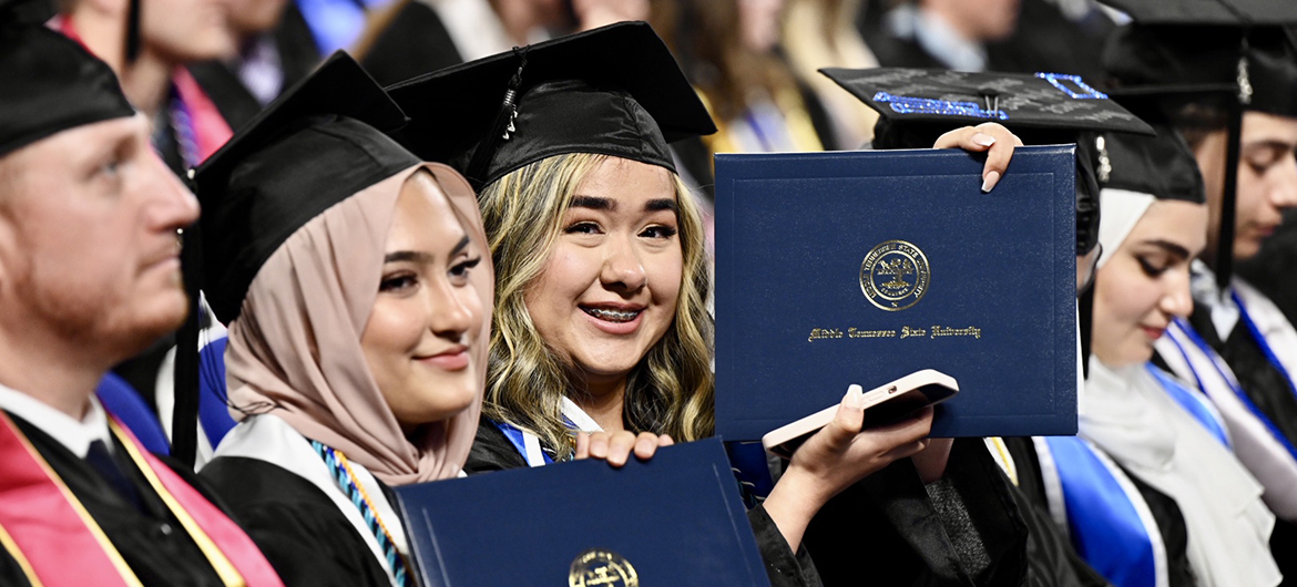 A happy Middle Tennessee State University graduate holds her hard-earned diploma after settling back into her seat inside Murphy Center during the university's spring 2022 evening commencement ceremony in this May file photo. More than 850 new members of MTSU's Class of 2022 are scheduled to receive their degrees Saturday, Aug. 6, during the university's summer 2022 commencement event. (MTSU file photo by James Cessna)