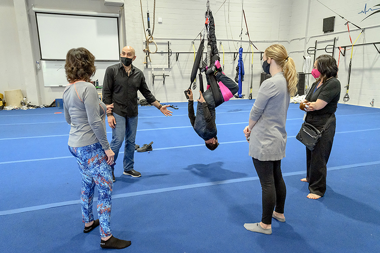 Then-graduate research assistant Rawsam Alasmar, second from left, watches as Framauro Fortich-Perez hangs upside down while using the PENDL, a device Fortich-Perez created to help improve physical flexibility and alleviate back pain. The MTSU Exercise Science program conducted evidence-based research into the PENDL. Observers during the March 26, 2021, demonstration in Alumni Memorial Gym are, from left, University Studies lecturer Debra Haber, Alasmar, PENDL Co-Founder and Director of Operations Brenna Rozario, and PENDL Business-to-Business Coordinator Patricia Lefler.