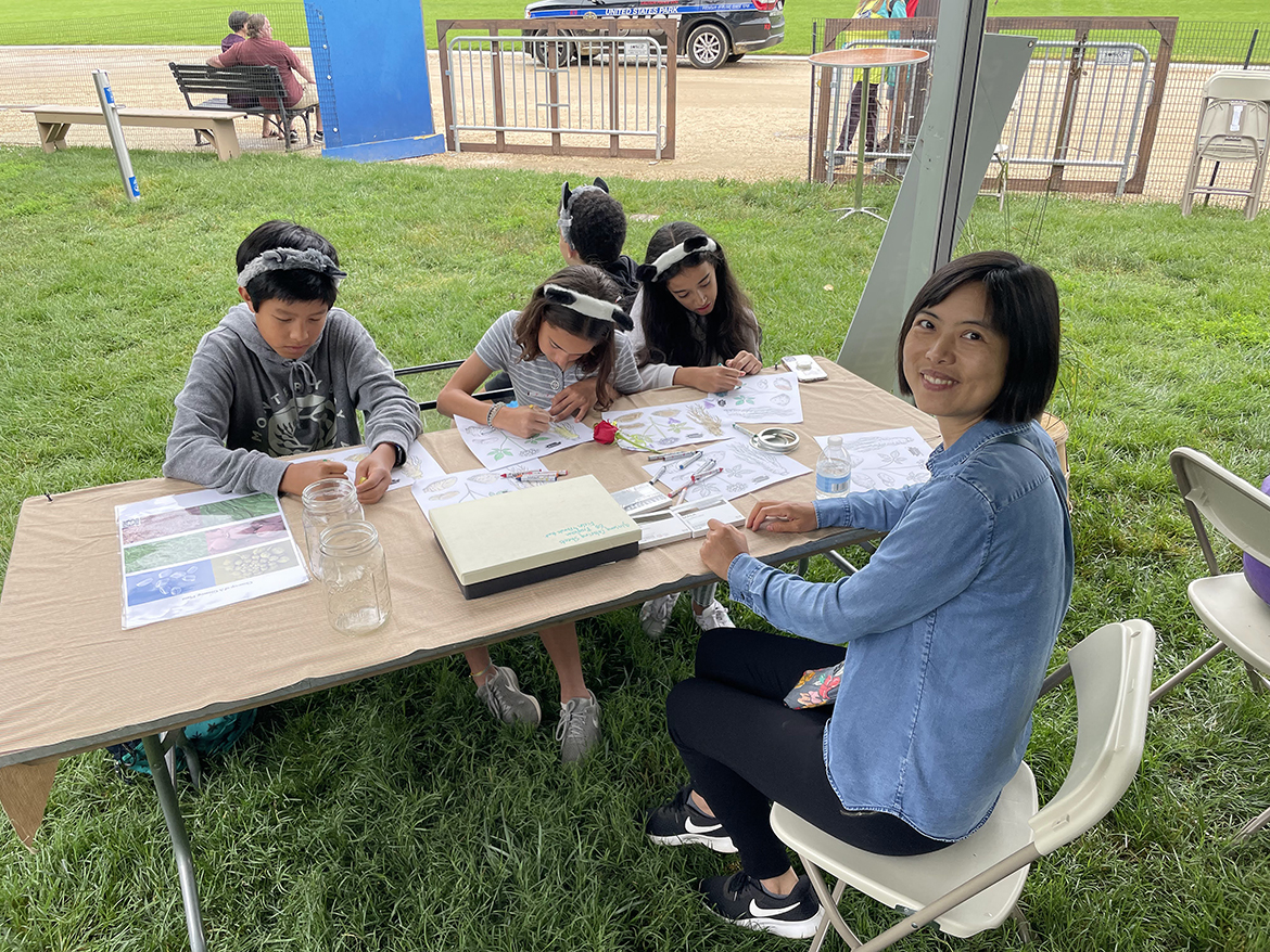 MTSU International Ginseng Institute Director Iris Gao, right, waits  while children attending the Smithsonian National Folklife Festival on the National Mall in Washington, D.C., earlier this year finish coloring projects related to native plants. The institute provides paper and crayons for youngsters at many events. (MTSU photo by Ethan Swiggart)