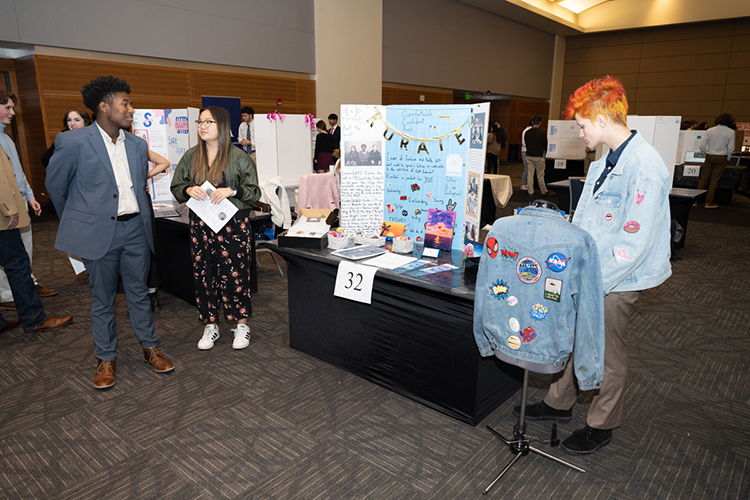 From front left, high school students Kamden Blackburn, Emma Collins and Connor Hughes of Franklin High School in Williamson County stand with the display for their fashion design business concept Kurated during MTSU’s seventh High School Entrepreneurship Fair held Nov. 16 in the Student Union Ballroom. (MTSU photo by James Cessna)