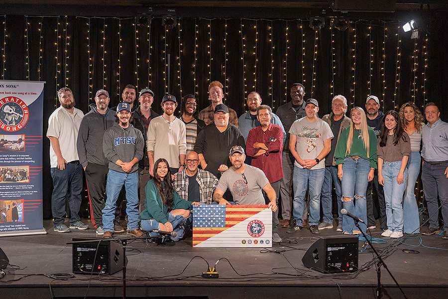 MTSU student veterans and student songwriters gather for a group photo with professional songwriters from Nashville in the Keathley University Center Theater at the close of the annual Operation Song writers' retreat at the university. Operation Song Executive Director Mike Byer is kneeling at center front with the wooden U.S. flag and organization and military branch logos. Seven trios, comprising a veteran, a student writer and a pro, spent the day turning the veterans' stories into music to share. MTSU's Charlie and Hazel Daniels Veterans and Military Family Center and the Commercial Songwriting Program have hosted the event since 2016. (MTSU photo by Cat Curtis Murphy)