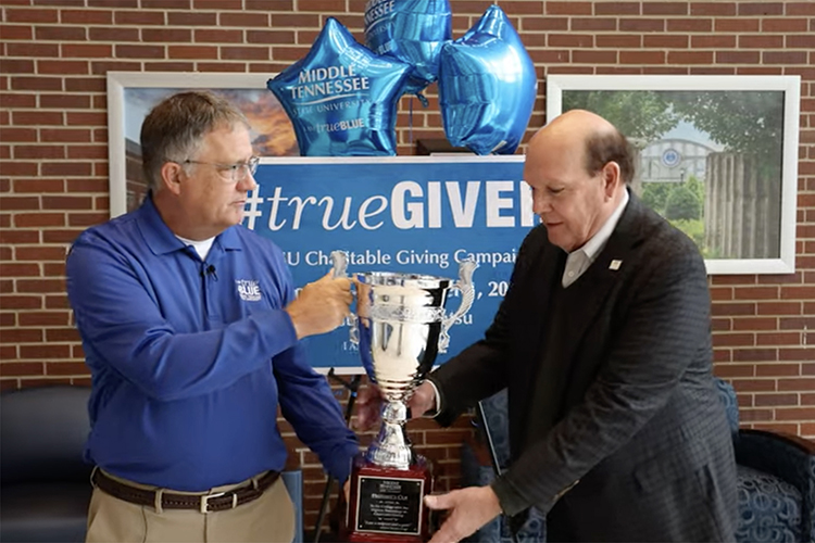 MTSU Provost Mark Byrnes, left, presents the Provost Cup to Jones College of Business Dean David Urban recently in the Cope Administration Building lobby to wrap up the 2022-23 MTSU Employee Charitable Giving Campaign. The Provost Cup is a friendly competition between academic units that is awarded to the college with the highest percentage of employee participation. The Jones College of Business has won the cup for 10 straight years. (From MTSU video screen capture)