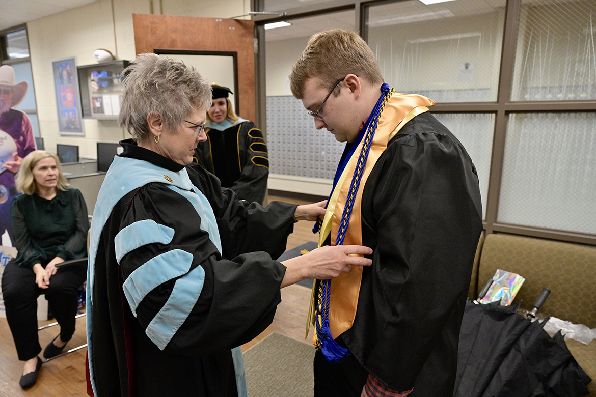 Deb Sells, left, Middle Tennessee State University vice president of Student Affairs and vice provost for Enrollment and Academic Services, helps adjust the stoles being worn by fall 2022 graduate Brad Trotter on Wednesday, Dec. 7, in the Charlie and Hazel Daniels Veterans and Military Family Center inside Keathley University Center. Looking on in the background are Wendy Trotter, left, and Daniels Center Director Hilary Miller. The Daniels Center hosted a small celebration for the Trotter family since Chaz Trotter, Brad’s father and a U.S. Navy veteran, will not attend commencement and, instead, watch the commencement ceremony on the university’s livestream channel on True Blue TV. Chaz Trotter was diagnosed with ALS, or Lou Gehrig’s disease, in 2019. (MTSU photo by Andy Heidt)