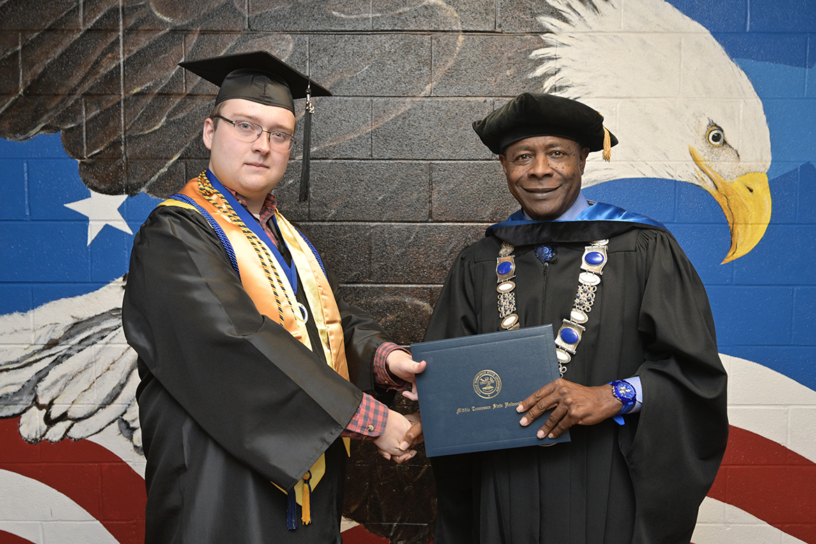 Middle Tennessee State University President Sidney A. McPhee, right, congratulates and awards an MTSU diploma to fall 2022 graduate Brad Trotter on Wednesday, Dec. 7, at the patriotic mural outside the the Charlie and Hazel Daniels Veterans and Military Family Center inside Keathley University Center. The Daniels Center invited McPhee and Deb Sells, vice president of Student Affairs, to celebrate the occasion with the Trotter family. Chaz Trotter, Brad’s father and a U.S. Navy veteran, was diagnosed with ALS in 2019. A political science (pre-law concentration) major, Brad Trotter will graduate at 2 p.m. Saturday, Dec. 10, in Murphy Center. (MTSU photo by Andy Heidt)