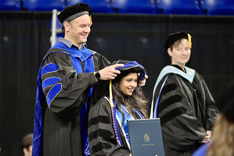 MTSU biology professor David Nelson carefully arranges Aarthi Subramani's new doctoral hood over her academic cap to signify her completion of her Ph.D. in molecular biosciences in Hale/Earle Arena inside Murphy Center during the university's Dec. 10 commencement ceremonies. MTSU presented 1,698 students with their degrees — 1,345 undergraduates and 353 graduate students — to mark the first graduation of its 112th academic year. (MTSU photo by Andy Heidt)