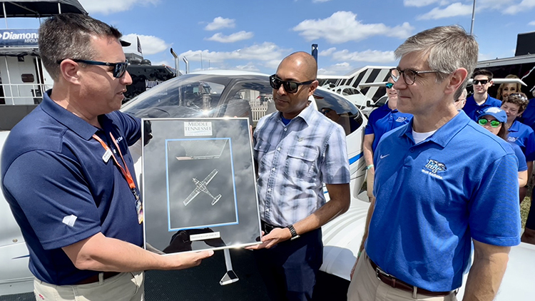 Trevor Mustard, head of sales and marketing for Diamond Aircraft, left, presents Middle Tennessee State University Aerospace Department Chair Chaminda Prelis with a special token of appreciation for the business relationship between the two entities Wednesday, March 29, 2023, at the Sun ’n Fun aviation event in Lakeland, Fla., where MTSU faculty and staff picked up the first of eight new Diamond DA40 XLT aircraft, in immediate background, to be added to the university’s fleet to train pilots. Also pictured is Greg Van Patten, dean of the College of Basic and Applied Sciences, right, and MTSU Aerospace faculty, flight instructor and student representatives, back right. (MTSU photo by Andrew Oppmann)