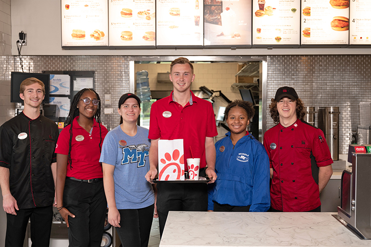 Middle Tennessee State University student and Murfreesboro Chick-fil-A employee Kaylin Garton, third from left, is shown here with some of her coworkers inside one of the Murfreesboro locations in this 2022 file promotional photo. Garton is among employees taking advantage of a partnership between the Noblitt family, owners of the local restaurant, and the university that provides tuition assistance to qualifying Chick-fil-A employees. (MTSU file photo by J. Intintoli)