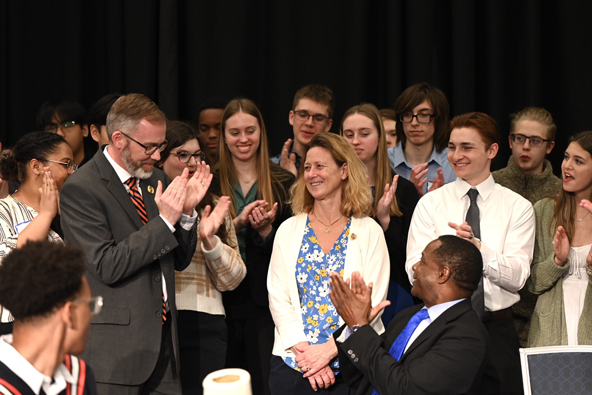 Led by Blackman High School Principal Justin Smith, left, and Middle Tennessee State University President Sidney A. McPhee, seated right, Blackman students applaud Kim Baumann, center, the dean for the Blackman Collegiate Academy. BCA has been, an eight-year partnership with the university. Smith, McPhee and Rutherford County Schools’ Director Jimmy Sullivan signed a renewal of  the memorandum of understanding between the high school and university. (MTSU photo by James Cessna)