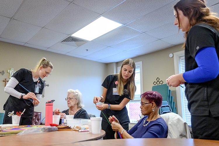 Middle Tennessee State University School of Nursing students Barbara Frizzell, far left, Insa Feldhusen, center, and Kaitlyn Beckstead, far right, guide members of the local Mindful Care adult day program in a crafting activity as part of a new partnership between the nonprofit and students in the Health and Gerontology course on March 13, 2023, in Murfreesboro, Tenn. (MTSU photo by J. Intintoli)