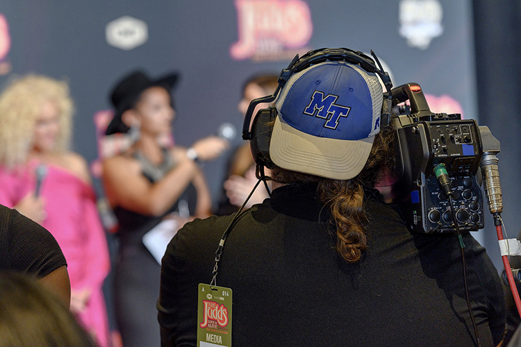 A Middle Tennessee State University student in an MTSU-branded hat films the university’s live broadcast of the student-fronted red-carpet show before “The Judds: Love is Alive – The Final Concert” on Nov. 3 at Murphy Center on MTSU’s campus. University students, faculty and alumni collaborated to work both in front of and behind the cameras on nearly every aspect of the made-for-TV concert set to air Saturday, April 29, on CMT. In the background holding the mic is student Liliana Manyara interviewing members of Little Big Town. (MTSU file photo by Cat Curtis Murphy)
